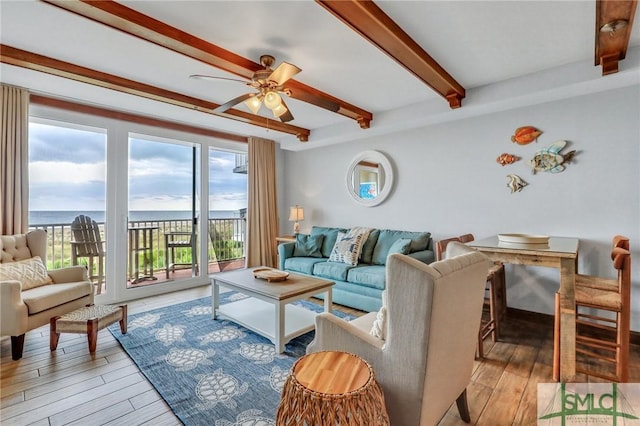 living area with beamed ceiling, a water view, light wood-style floors, and a ceiling fan