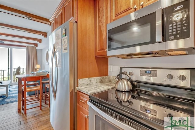 kitchen with light wood-type flooring, stainless steel appliances, light stone countertops, and brown cabinetry