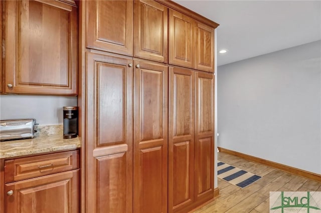 kitchen featuring light stone counters, brown cabinetry, baseboards, recessed lighting, and light wood-style floors