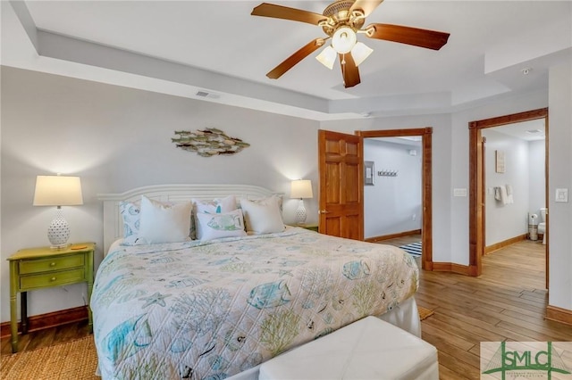 bedroom with wood finished floors, visible vents, baseboards, ceiling fan, and a raised ceiling