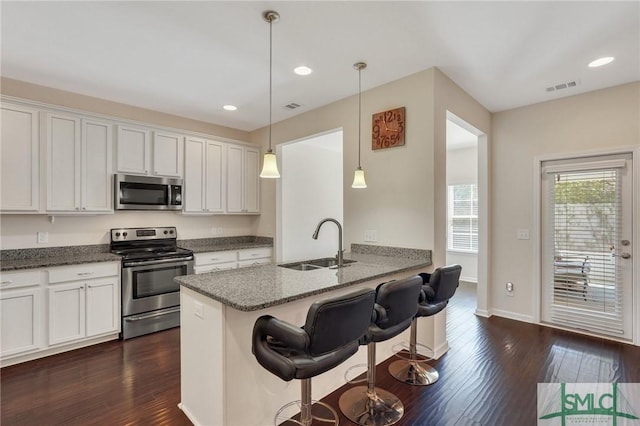 kitchen featuring dark wood-style floors, a sink, a breakfast bar, visible vents, and appliances with stainless steel finishes