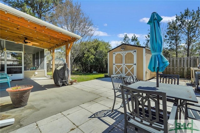 view of patio / terrace with a shed, an outbuilding, outdoor dining area, a sunroom, and a fenced backyard