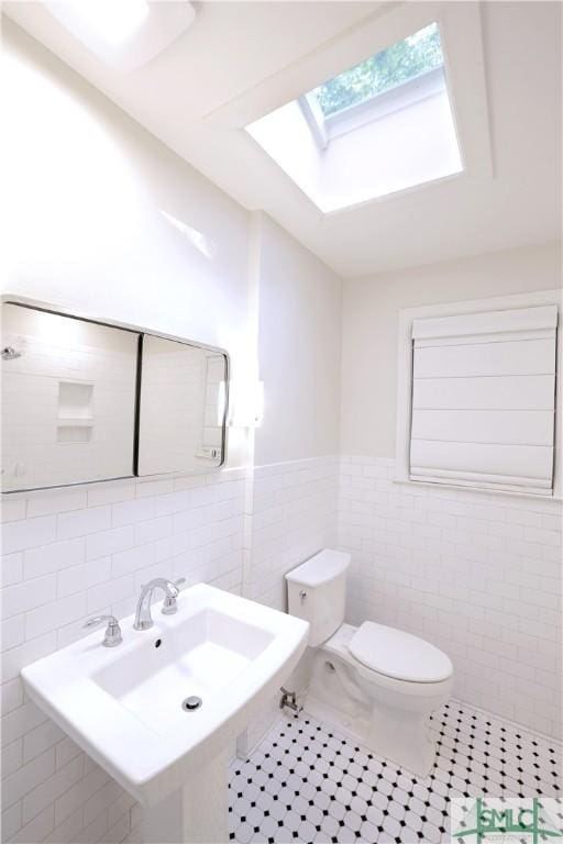 bathroom featuring a skylight, tile patterned floors, tile walls, a wainscoted wall, and toilet