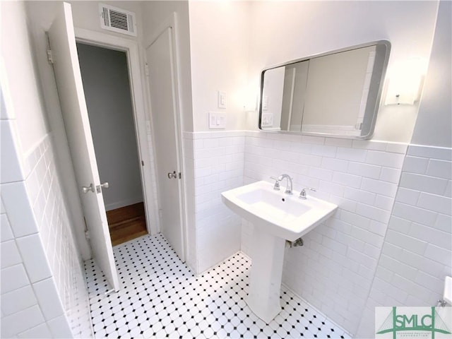 bathroom featuring a sink, visible vents, wainscoting, and tile walls