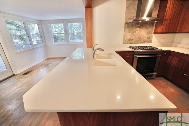 kitchen featuring light countertops, a sink, wall chimney range hood, and stainless steel range with gas cooktop