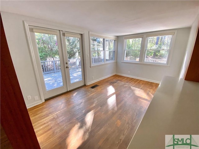 interior space with wood finished floors, french doors, plenty of natural light, and baseboards