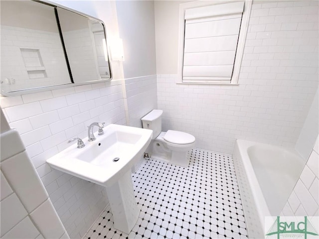 full bath with a tub to relax in, a wainscoted wall, toilet, tile walls, and tile patterned flooring