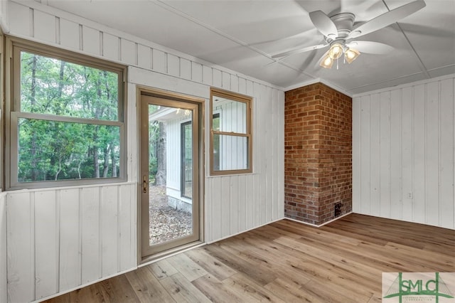interior space featuring a ceiling fan, a healthy amount of sunlight, wood finished floors, and wooden walls