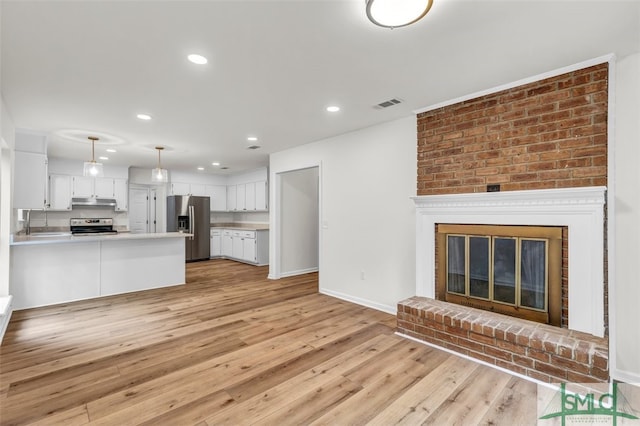 unfurnished living room featuring light wood finished floors, a sink, baseboards, recessed lighting, and visible vents