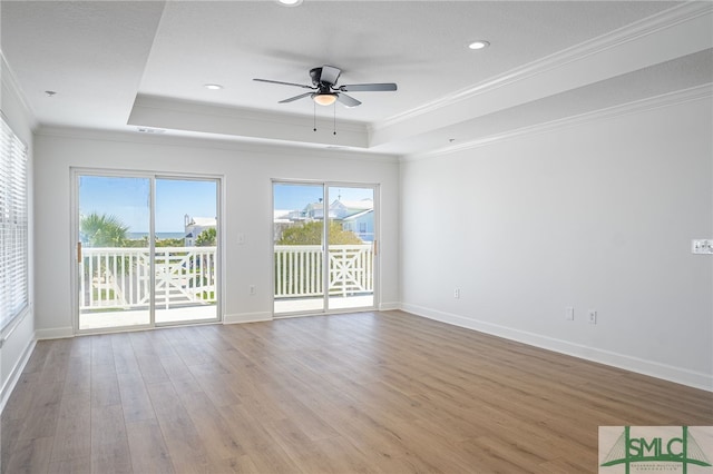 unfurnished living room featuring plenty of natural light, light wood-type flooring, ornamental molding, and a raised ceiling
