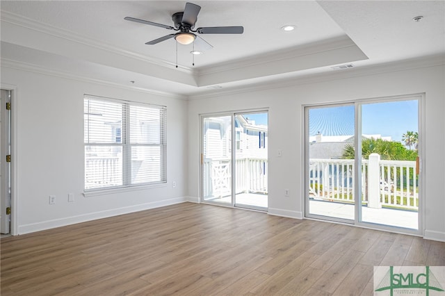 unfurnished living room with crown molding, a wealth of natural light, a tray ceiling, visible vents, and light wood finished floors