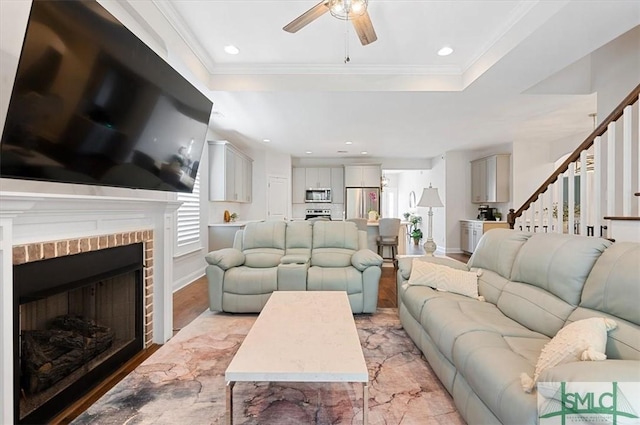 82 Rimmon Ct, Richmond Hill, GA 31324 - living room with a tray ceiling, stairway, ornamental molding, ceiling fan, and a brick fireplace
