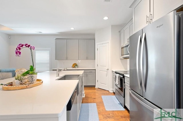 82 Rimmon Ct, Richmond Hill, GA 31324 - kitchen with light wood-type flooring, gray cabinets, a center island with sink, a sink, and appliances with stainless steel finishes