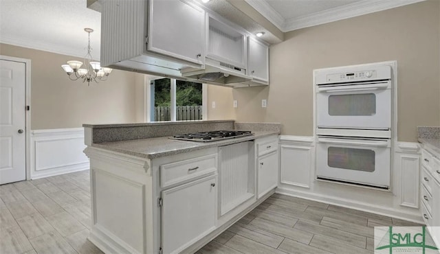 kitchen with light countertops, crown molding, white double oven, a chandelier, and a peninsula