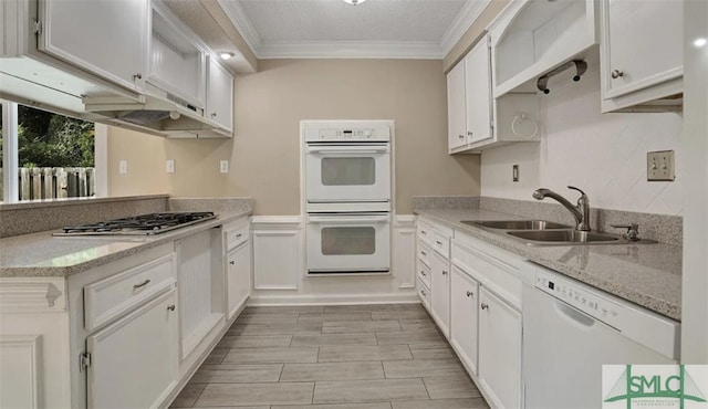 kitchen with white appliances, ornamental molding, white cabinetry, a sink, and light stone counters