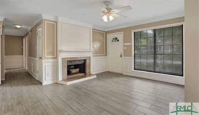 unfurnished living room featuring a wainscoted wall, a fireplace, ceiling fan, wood finished floors, and ornamental molding