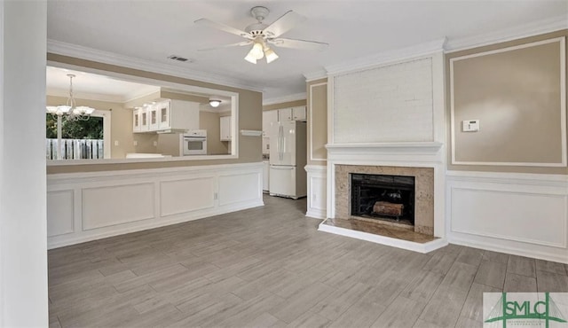 unfurnished living room with crown molding, ceiling fan with notable chandelier, a fireplace with raised hearth, a decorative wall, and wood tiled floor