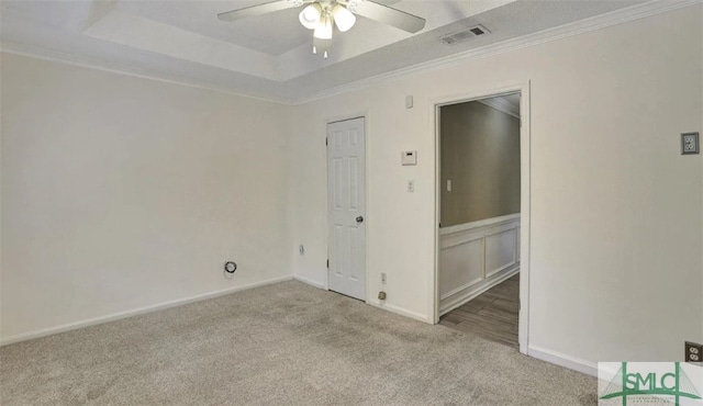 unfurnished room with a tray ceiling, carpet, a ceiling fan, visible vents, and ornamental molding