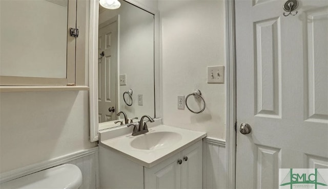 bathroom featuring a wainscoted wall, a decorative wall, toilet, and vanity