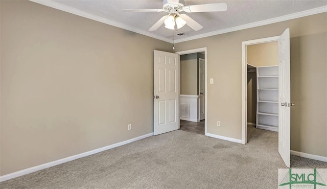 unfurnished bedroom with crown molding, a spacious closet, carpet, baseboards, and visible vents