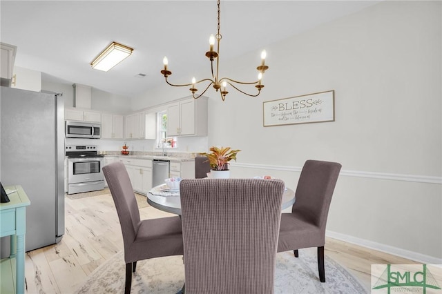 dining room featuring baseboards, vaulted ceiling, light wood-style floors, and a chandelier