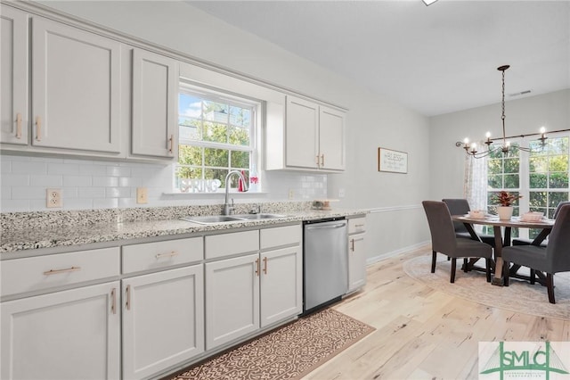 kitchen with stainless steel dishwasher, a sink, light wood-style floors, backsplash, and a notable chandelier