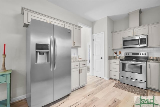 kitchen with light wood-style flooring, baseboards, light stone countertops, appliances with stainless steel finishes, and backsplash