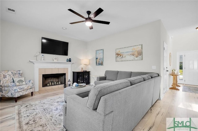 living area featuring visible vents, ceiling fan, light wood-style flooring, and a tiled fireplace