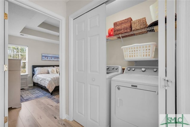 clothes washing area with washer and clothes dryer, visible vents, and light wood-style flooring