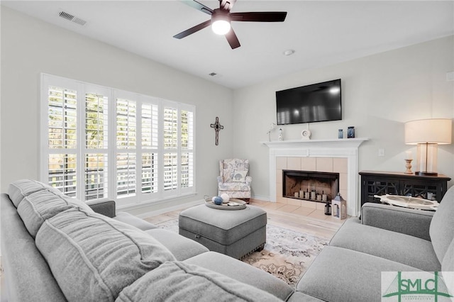 living room featuring baseboards, visible vents, a ceiling fan, a fireplace, and wood finished floors