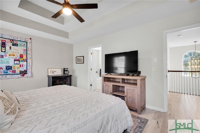 bedroom featuring a raised ceiling, baseboards, and light wood-style floors