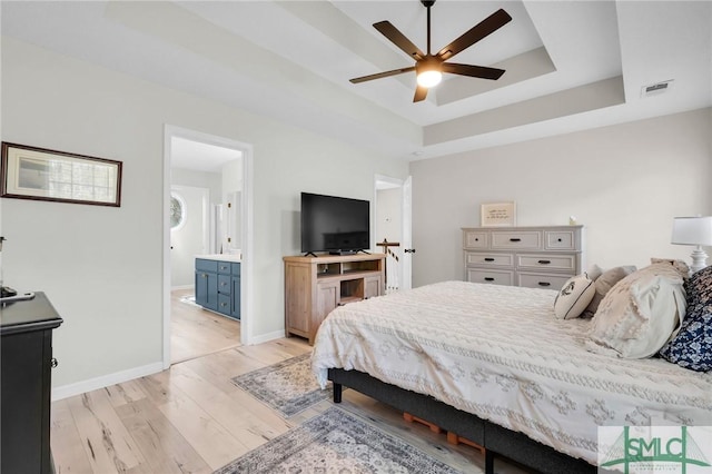 bedroom featuring light wood-type flooring, baseboards, a raised ceiling, connected bathroom, and visible vents