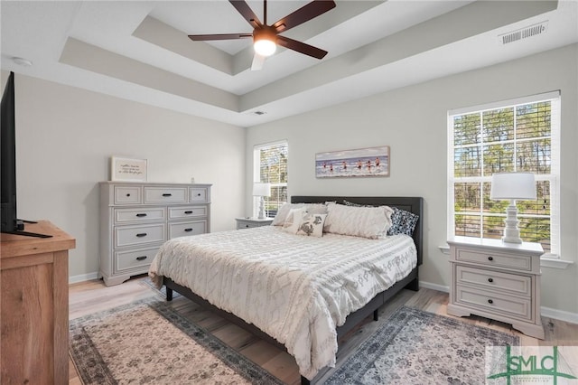 bedroom with light wood-style flooring, a tray ceiling, baseboards, and visible vents
