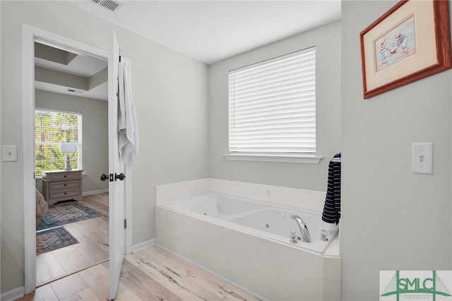bathroom with a tub with jets, visible vents, baseboards, and wood finished floors