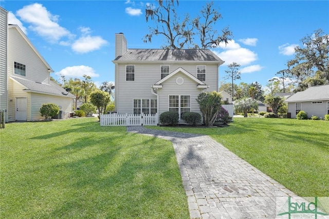 rear view of property with a lawn, a chimney, and fence