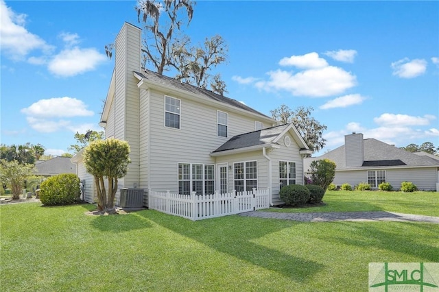 rear view of house with a chimney, central AC unit, fence, and a yard