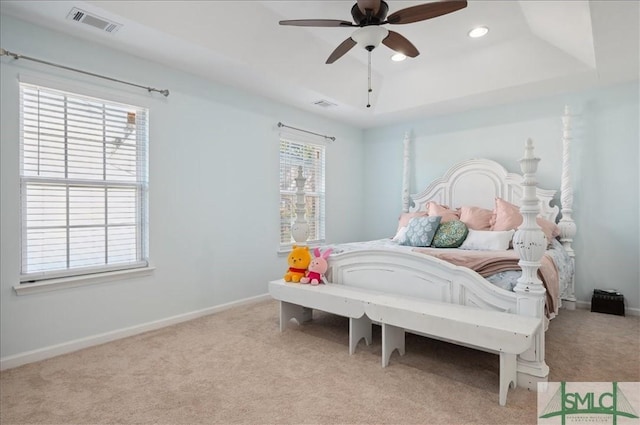 carpeted bedroom featuring visible vents, multiple windows, and a raised ceiling