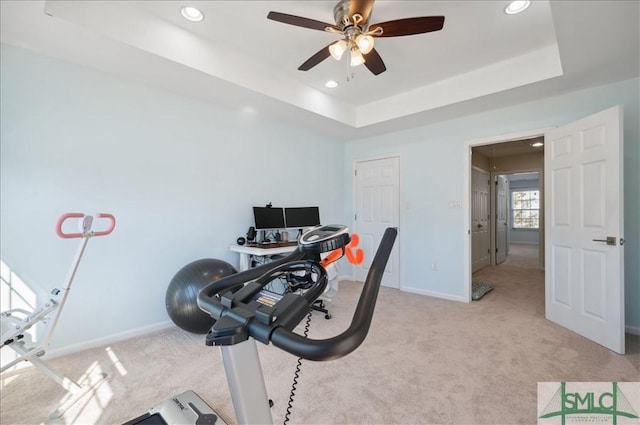 exercise room featuring a raised ceiling, baseboards, light colored carpet, and ceiling fan