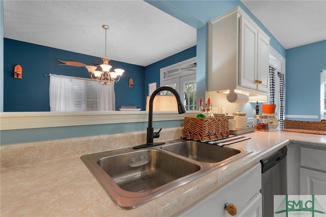 kitchen featuring white cabinets, dishwasher, a sink, pendant lighting, and a notable chandelier