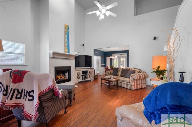 living room with a towering ceiling, a tile fireplace, ceiling fan, and wood finished floors
