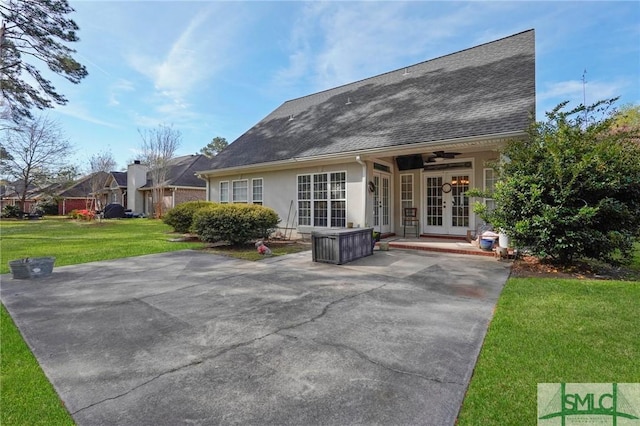 rear view of house with stucco siding, roof with shingles, french doors, ceiling fan, and a yard