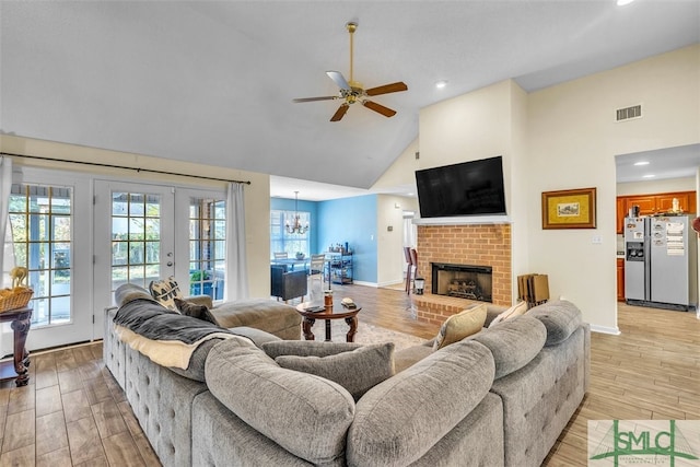 living room with high vaulted ceiling, ceiling fan, french doors, a fireplace, and light wood-type flooring