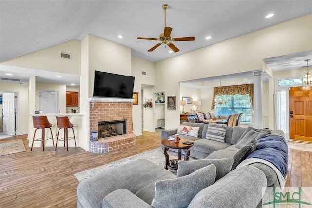 living room featuring high vaulted ceiling, light wood-style floors, a ceiling fan, a brick fireplace, and recessed lighting