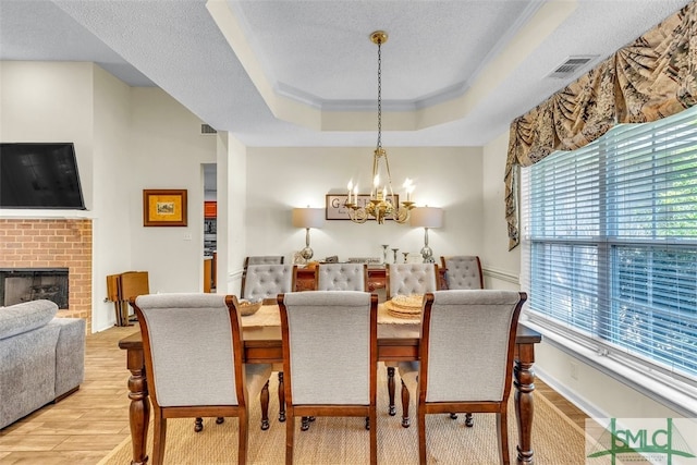 dining room with a chandelier, healthy amount of natural light, light wood finished floors, a tray ceiling, and a textured ceiling