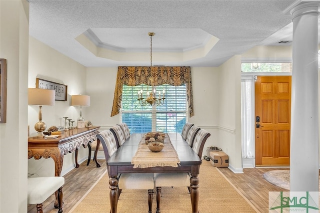 dining space featuring a chandelier, light wood-style flooring, a textured ceiling, a raised ceiling, and baseboards