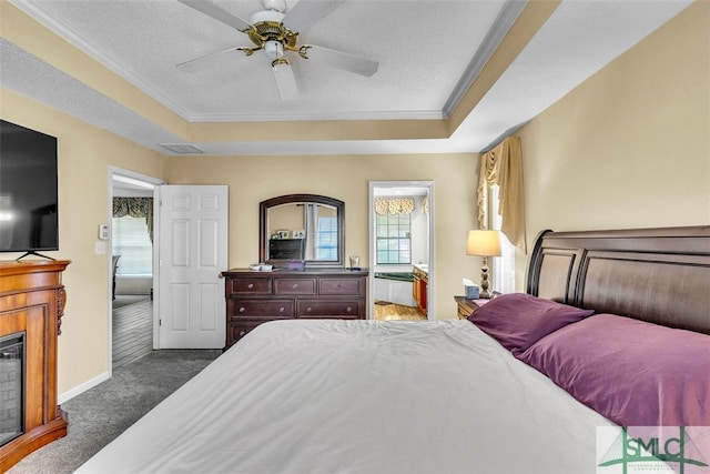 carpeted bedroom with a tray ceiling, crown molding, baseboards, a glass covered fireplace, and ceiling fan