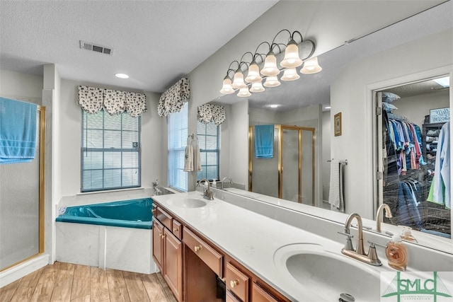 bathroom with a stall shower, a textured ceiling, double vanity, a bath, and wood finished floors