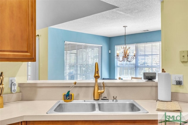 kitchen featuring a sink, a textured ceiling, light countertops, a chandelier, and pendant lighting