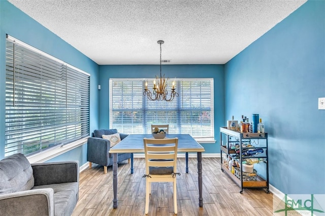 dining space featuring a chandelier, a textured ceiling, wood finished floors, and baseboards