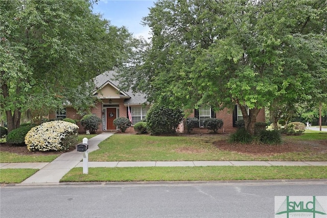 view of property hidden behind natural elements featuring a front yard and brick siding